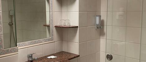 A bathroom with a granite sink, a mirror, a shower, and a towel rack.