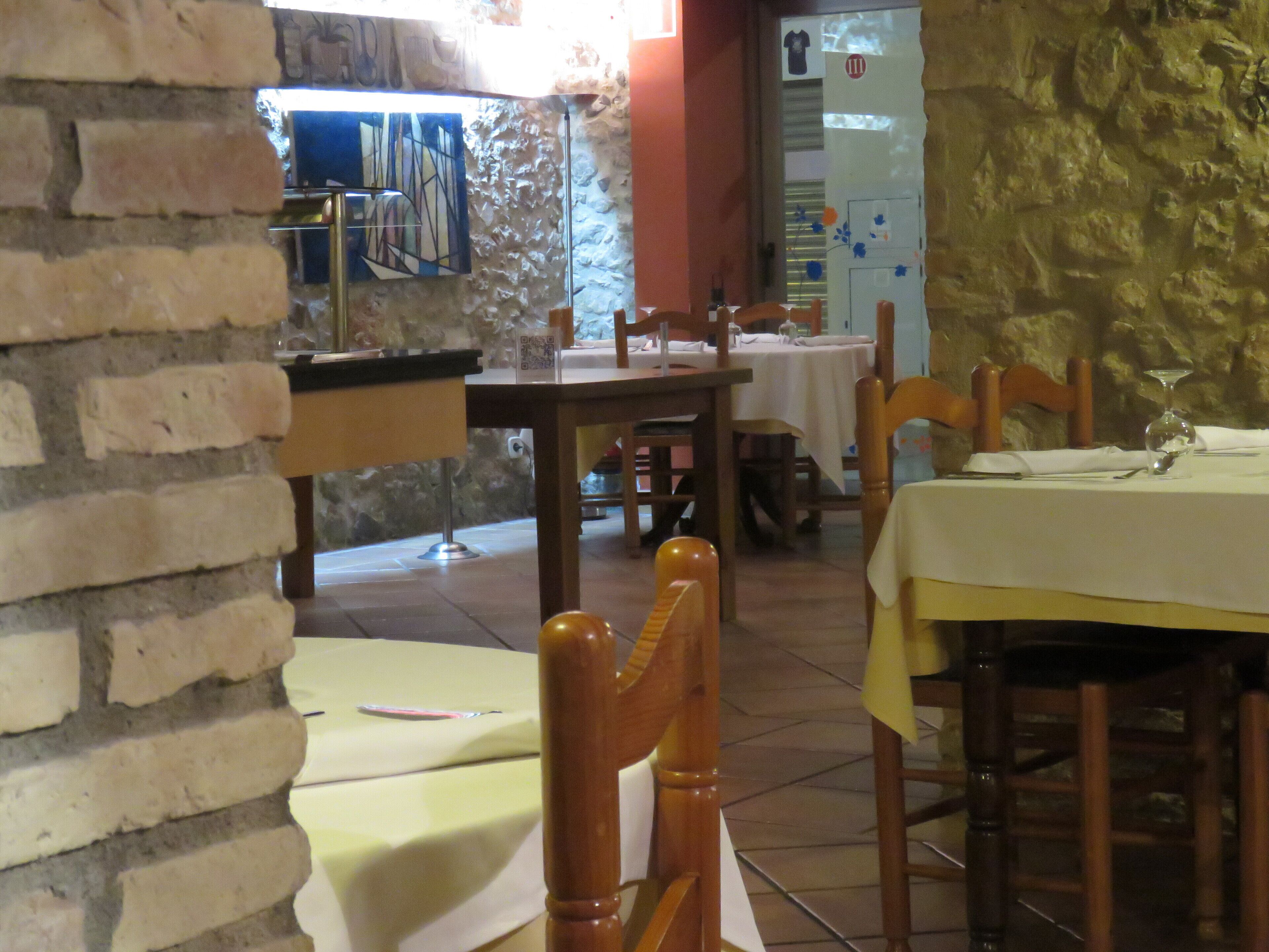 Interior de restaurante con paredes de ladrillo, sillas y mesas de madera preparadas para comer.