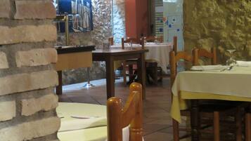 Interior de restaurante con paredes de ladrillo, sillas y mesas de madera preparadas para comer.