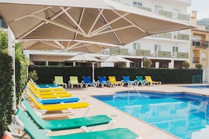 A swimming pool area with multiple lounge chairs and umbrellas.