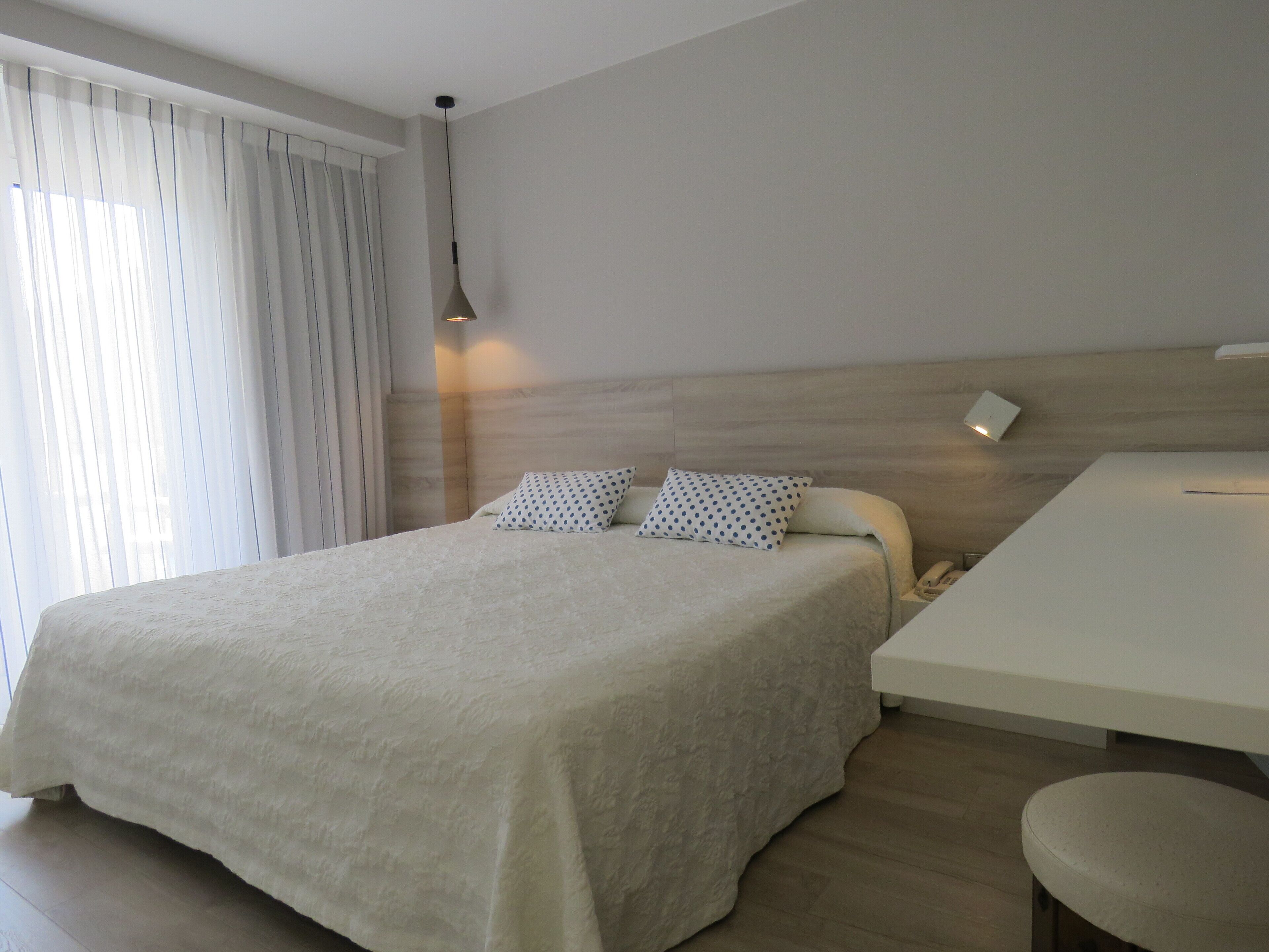 Quarto de hotel moderno com uma cama grande, uma mesinha de cabeceira e uma escrivaninha.