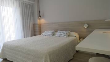 Quarto de hotel moderno com uma cama grande, uma mesinha de cabeceira e uma escrivaninha.