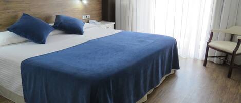 Una cama bien hecha con ropa de cama azul, un cabecero de madera y una mesita de noche con un teléfono.
