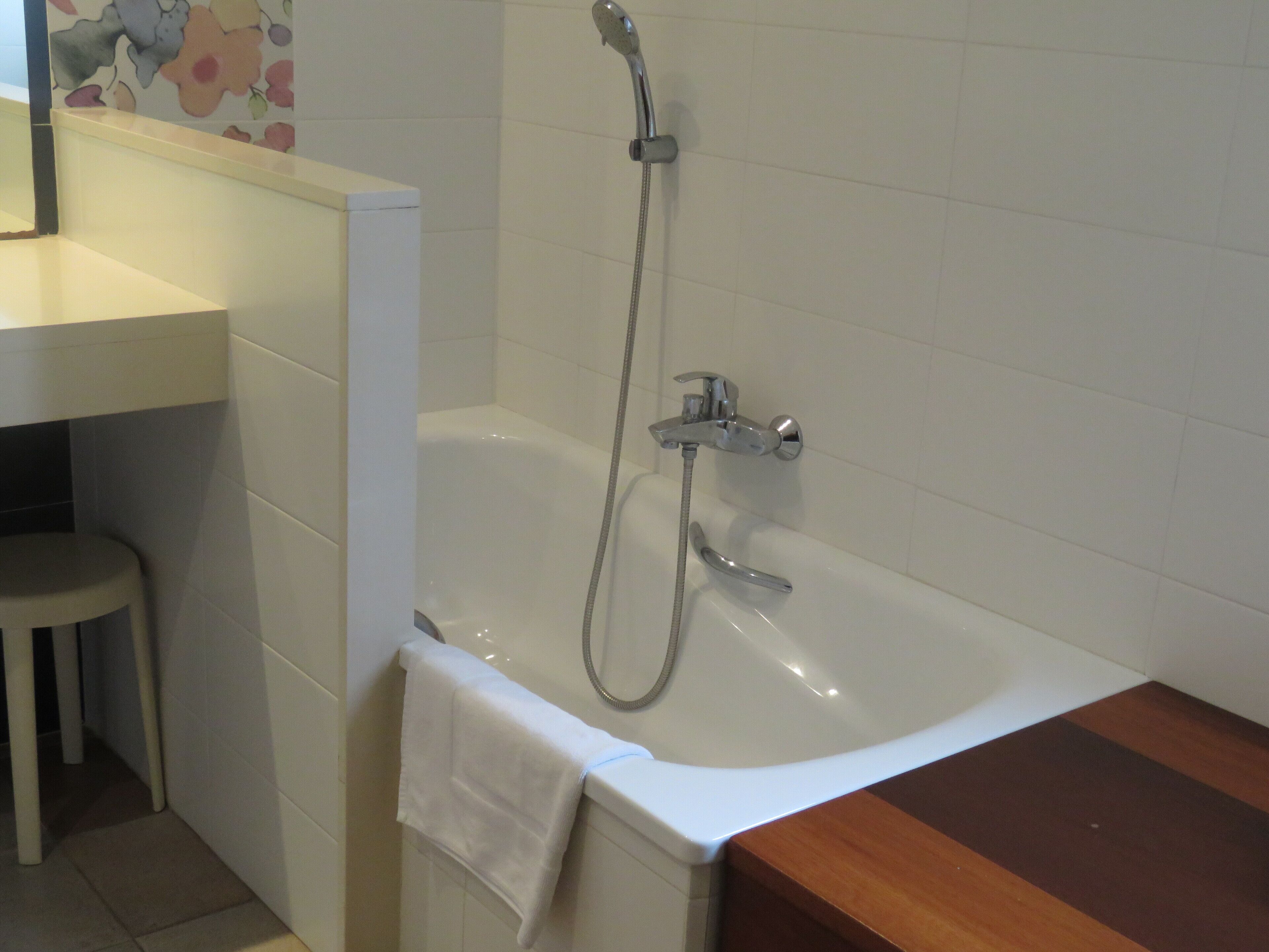 A bathroom with a white bathtub, a wooden vanity, and a small stool.