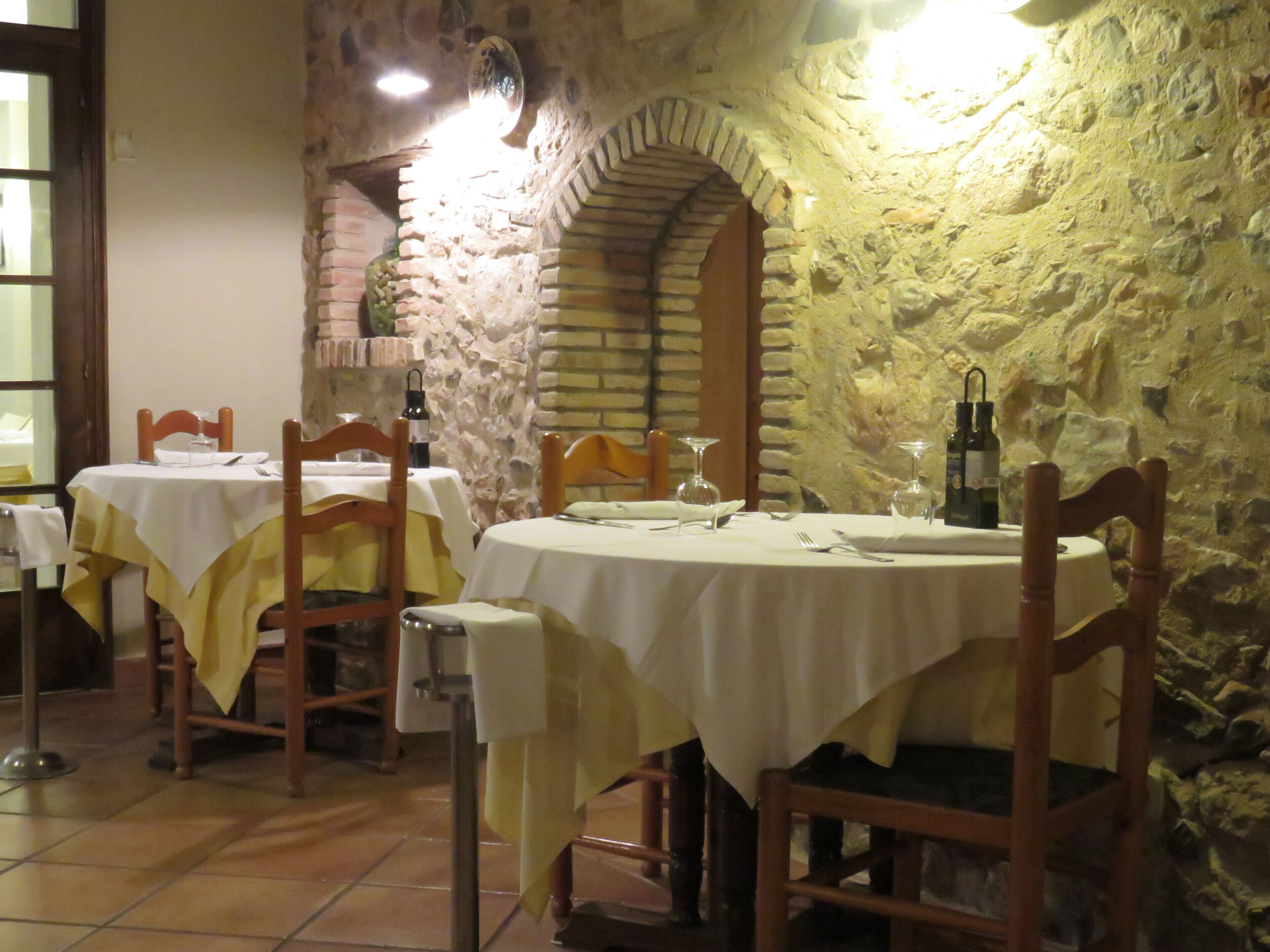 A restaurant with stone walls and wooden furniture. Tables are set with white tablecloths and wine glasses.