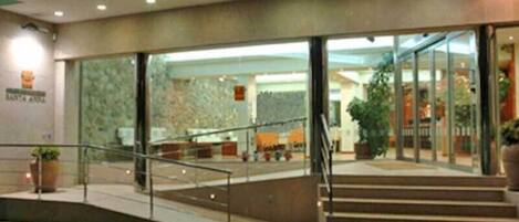 A hotel entrance with a glass facade, a staircase leading to the entrance, and a potted plant on the left.