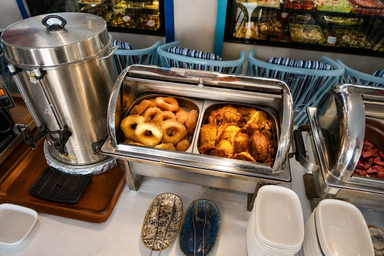 A buffet setup with a coffee pot, trays of fried chicken, and onion rings.
