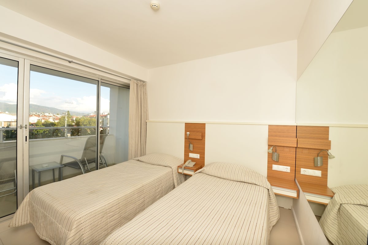 Een hotelkamer met twee bedden, een balkon met een glazen deur en uitzicht op de stad.