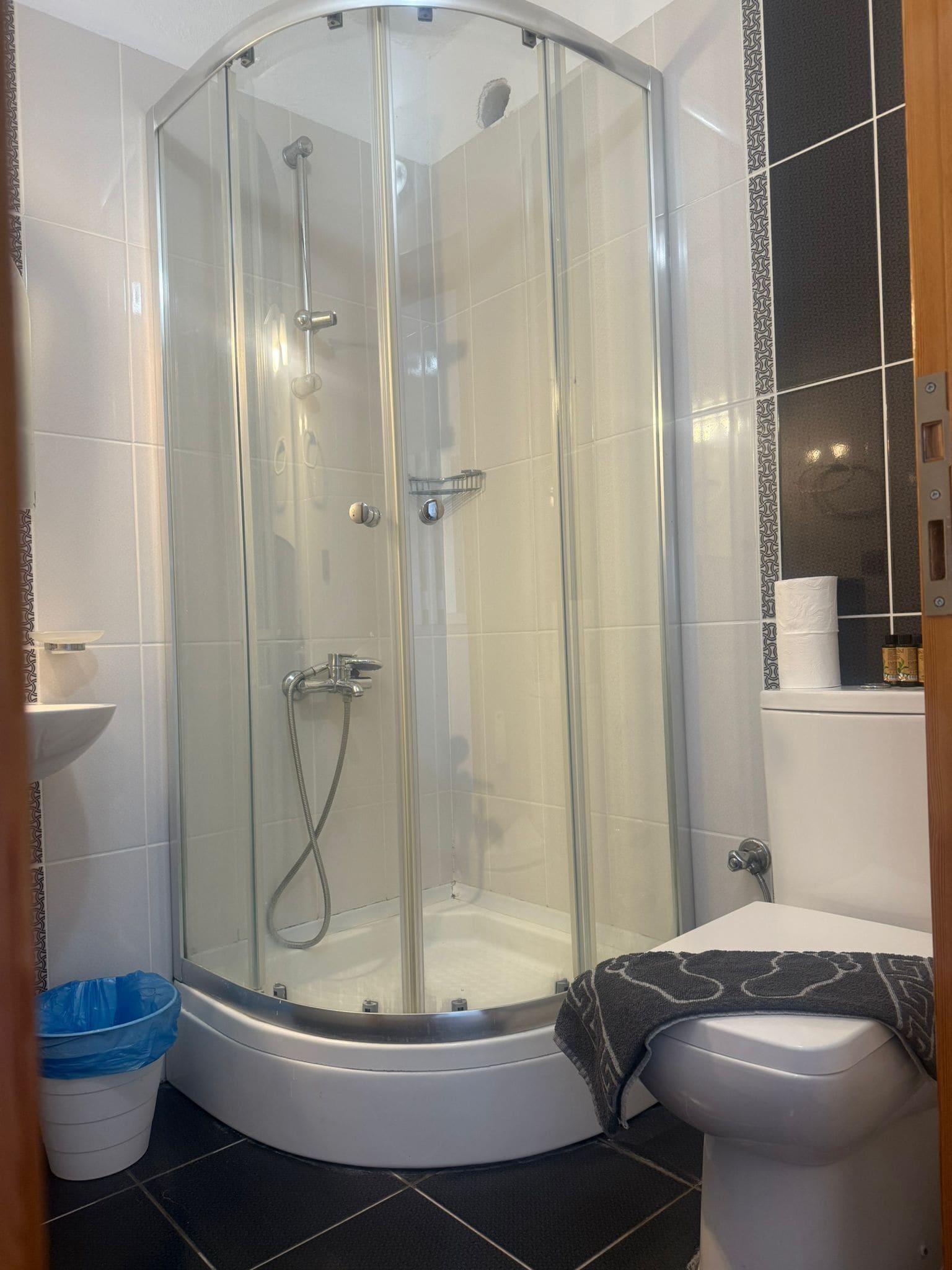 A glass-enclosed shower with a bathtub, a toilet, and a trash bin.