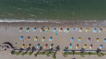 An aerial view of a beach with rows of colorful umbrellas and beach chairs, a stage area, and palm trees.