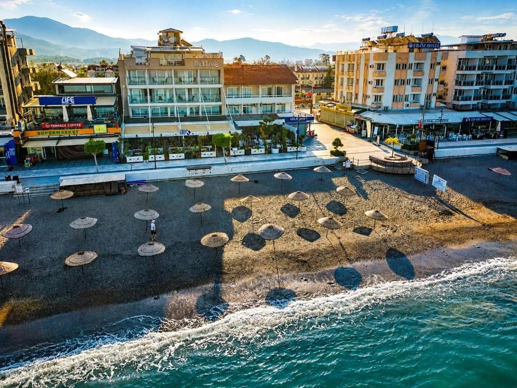 Une zone aménagée au bord de la plage, avec des parasols, une vue sur la mer et des bâtiments en arrière-plan.