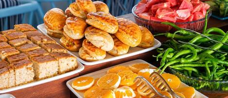 A buffet table with various food items including pastries, watermelon, green beans, and orange slices.