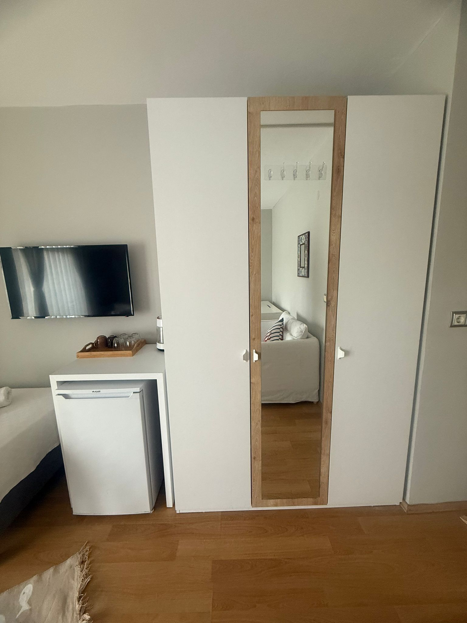 A compact room with a bed, a small white desk, a television, and a wardrobe.