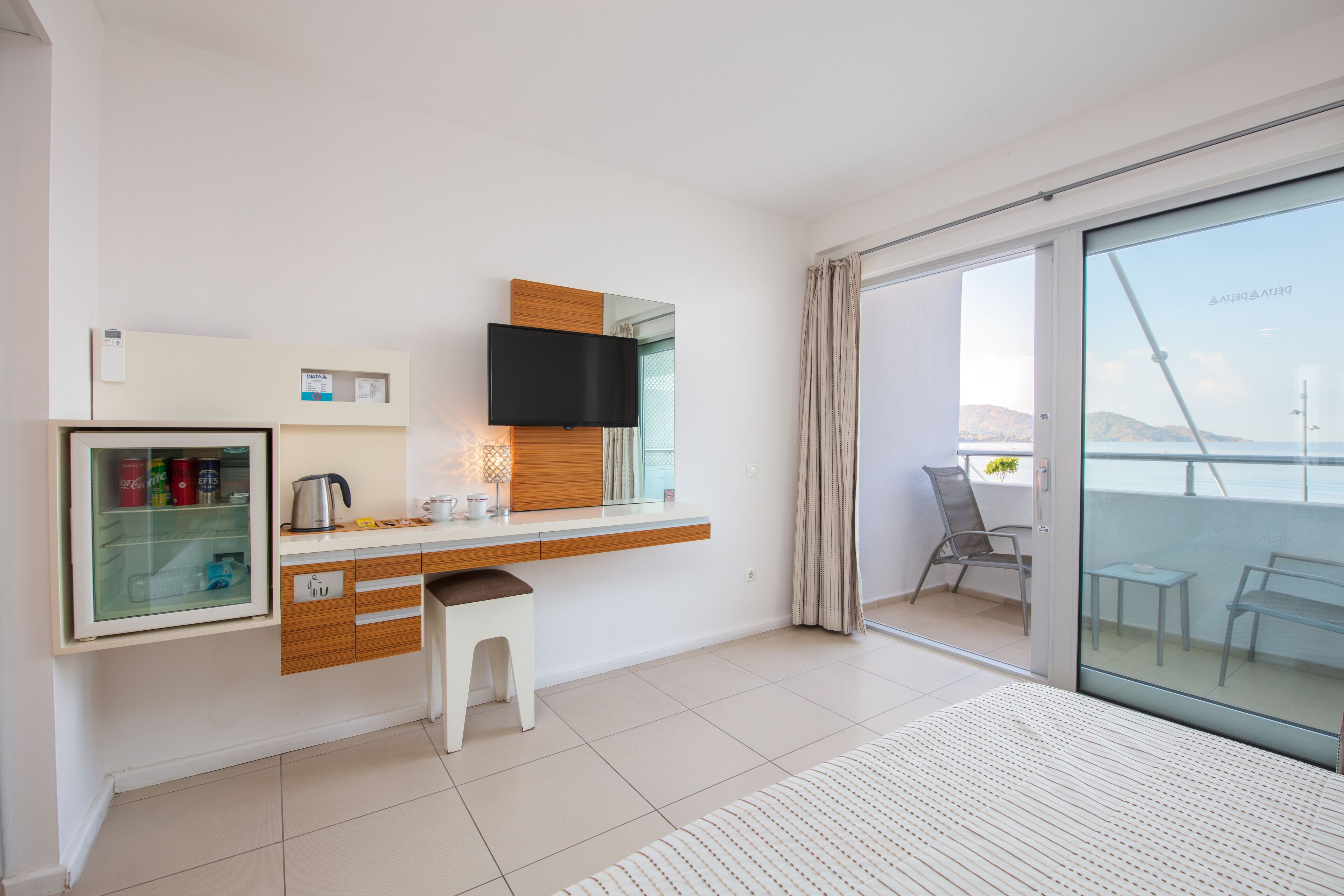 Habitació d'hotel moderna amb cuineta, televisió de pantalla plana, porta corredissa de vidre a un balcó i un llit amb col·cha de ratlles.