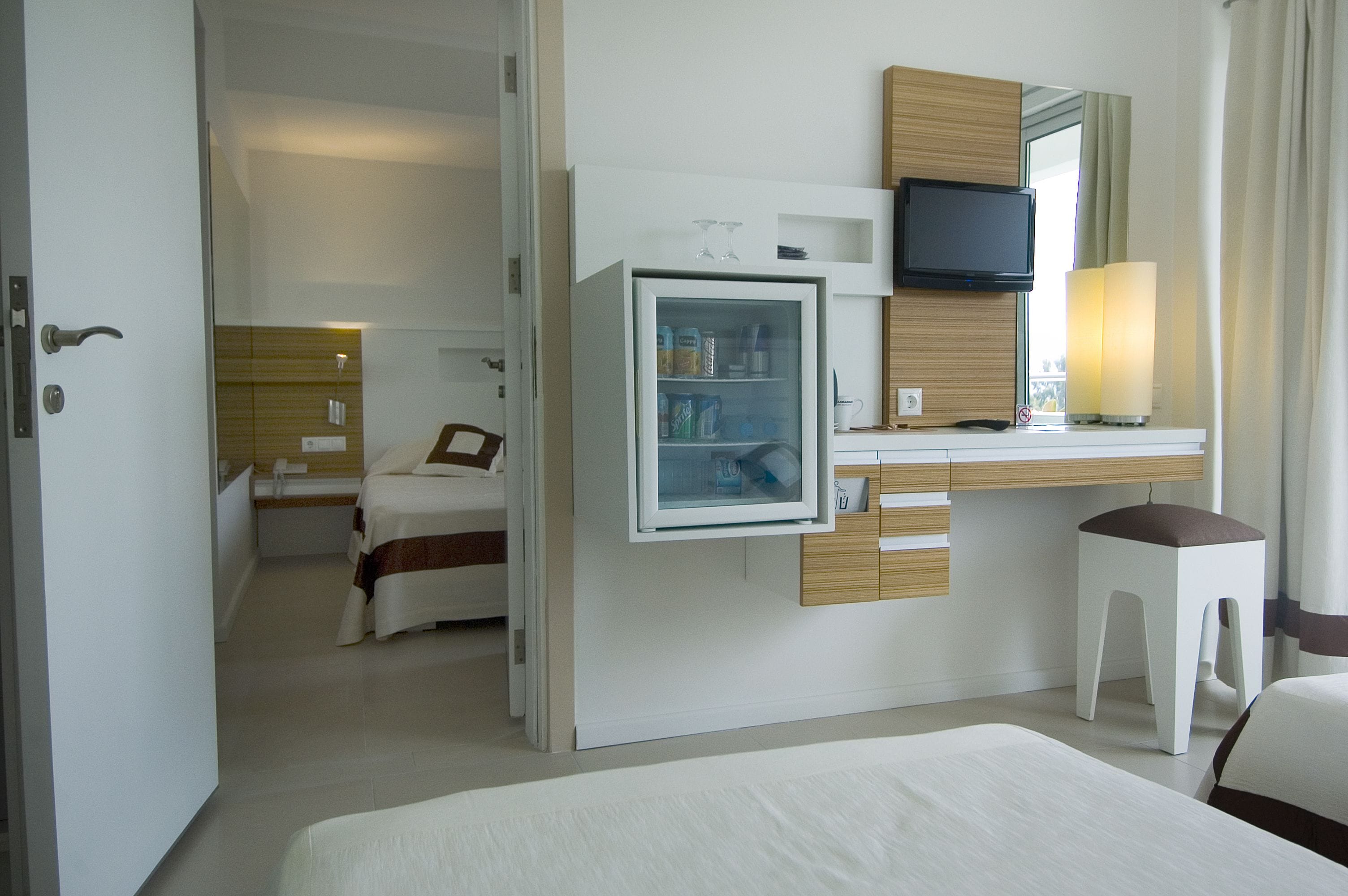 Ein Hotelzimmer mit einem Bett, einem kleinen Schreibtisch mit Fernseher, einem Kühlschrank und einem Fenster mit Vorhängen.