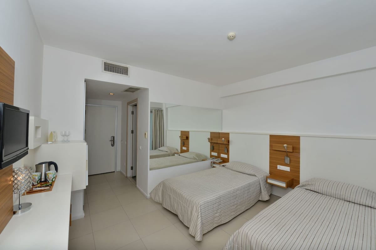 Een hotelkamer met een televisie, een bureau met een lamp, een bed, een spiegel en een deur die naar een andere kamer leidt.