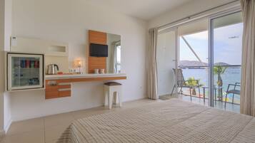 Une chambre d’hôtel moderne équipée d’un lit, d’une télévision, d’un minibar, d’un petit tabouret et d’un balcon avec vue sur la mer.