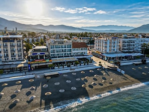 Een kusthotel met meerdere verdiepingen, terras en een strand voorzien van parasols.