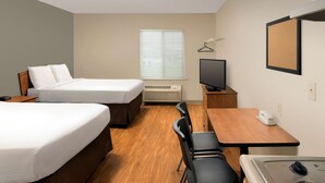 Een hotelkamer met twee bedden, een bureau met stoel, een televisie, een klein tafeltje met telefoon en een kitchenette met fornuis.