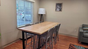 Een vergaderruimte met een houten tafel en metalen stoelen, een staande lamp, een grijze bank en een kamerbreed tapijt met dessin.