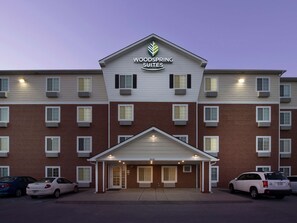 Un hotel de diverses plantes amb entrada central, aparcament i un cartell que diu "Woodspring Suites".