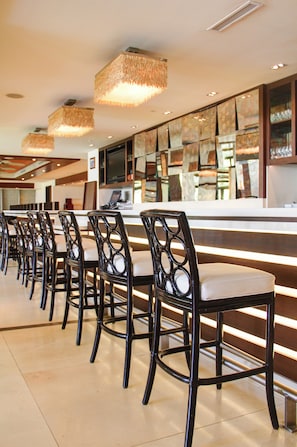 A long row of black chairs with white cushions, a counter with a glass top, and hanging woven light fixtures.