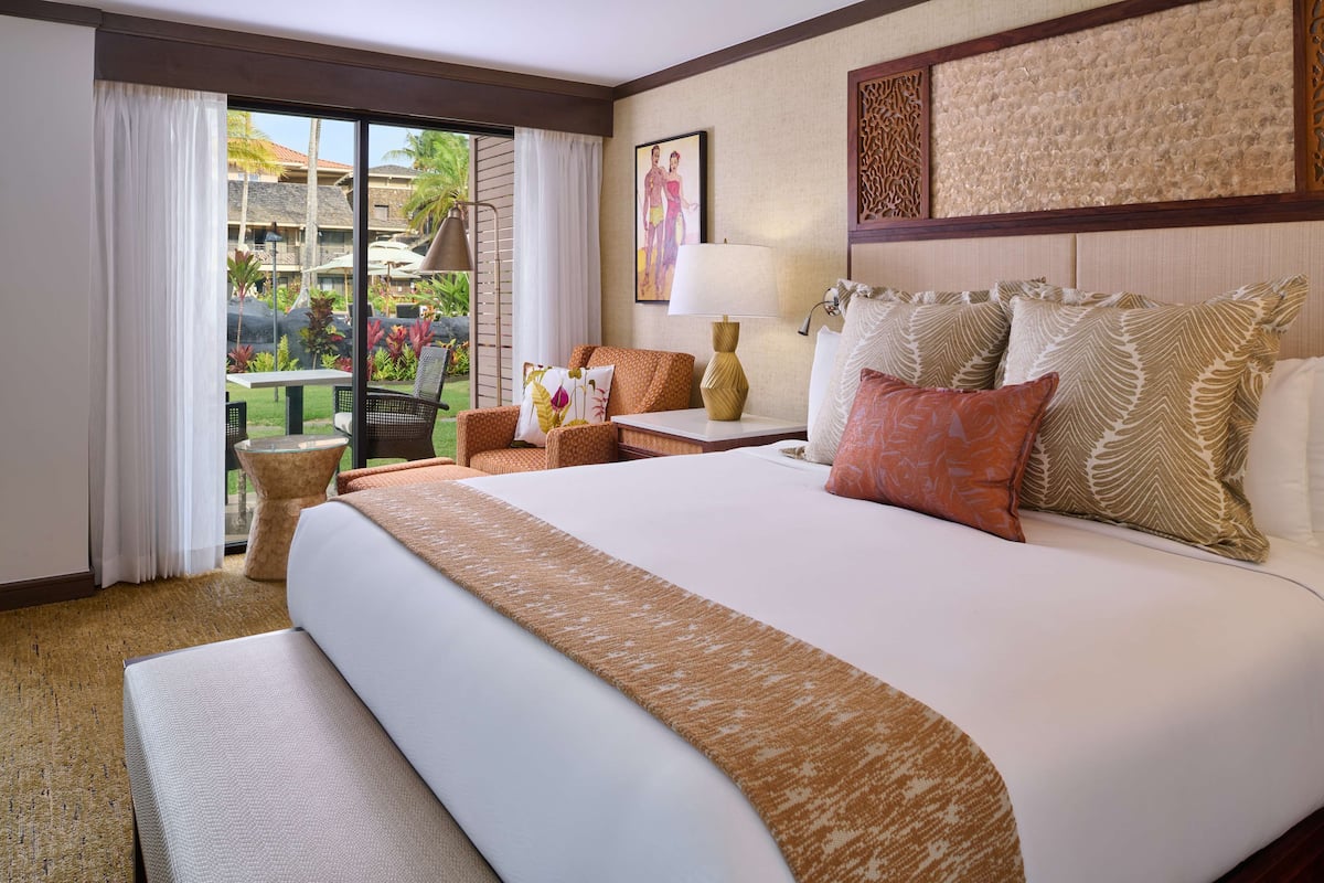 A hotel room with a large bed, a small table, a chair, and a view of the outdoors.