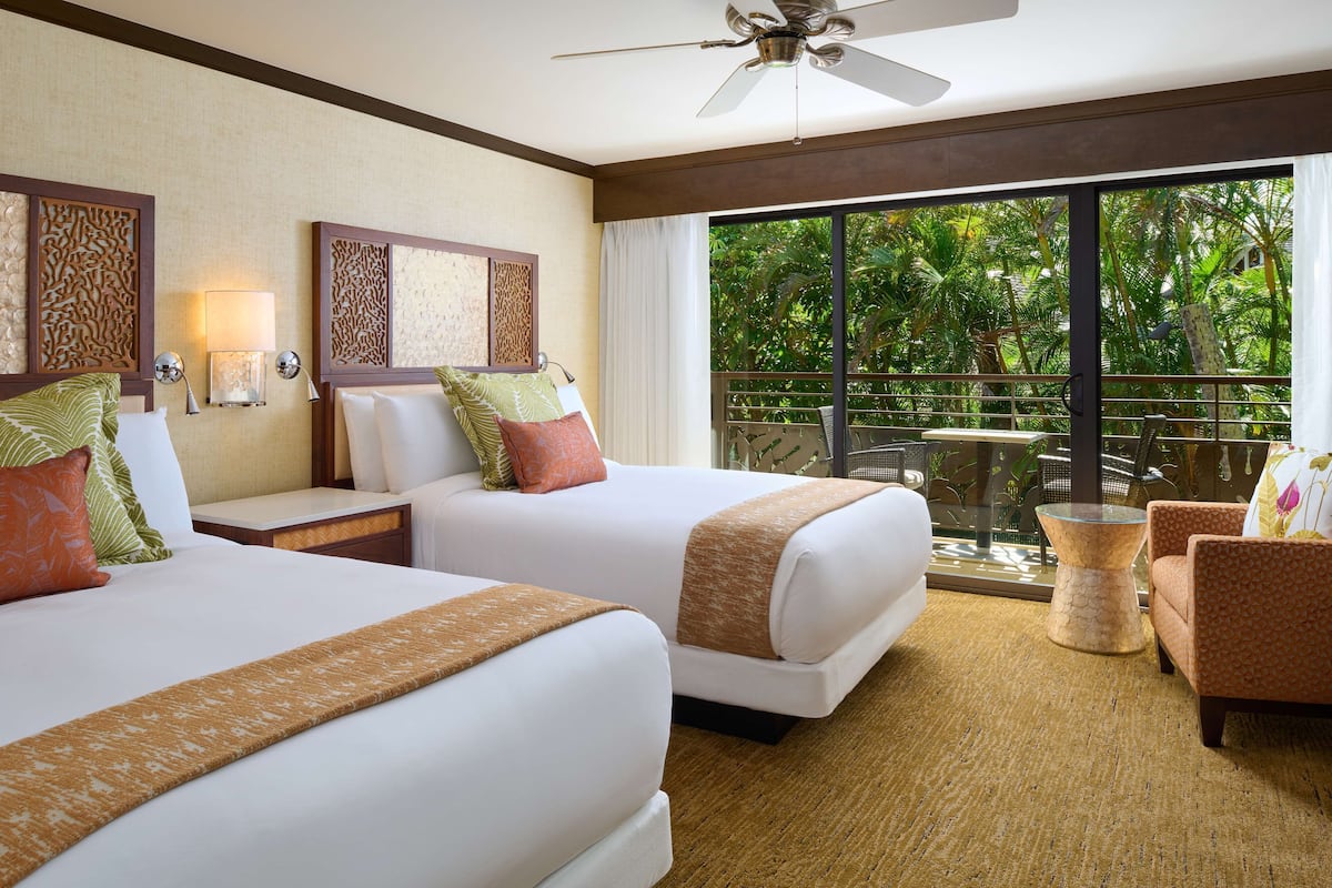 A hotel room with two beds, a balcony with a glass door, and a ceiling fan.