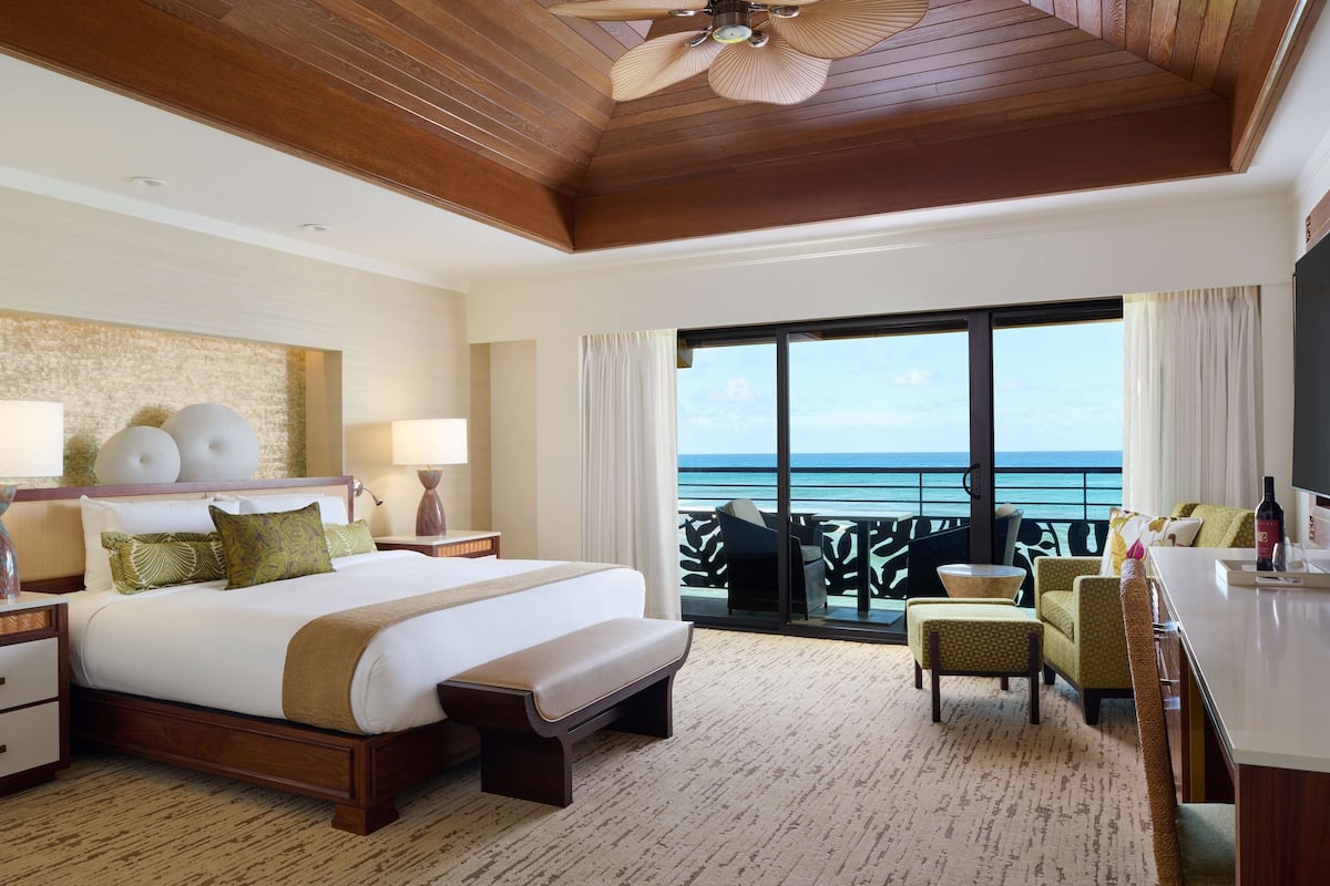 A hotel room with a large bed, a desk, a chair, and a view of the ocean.