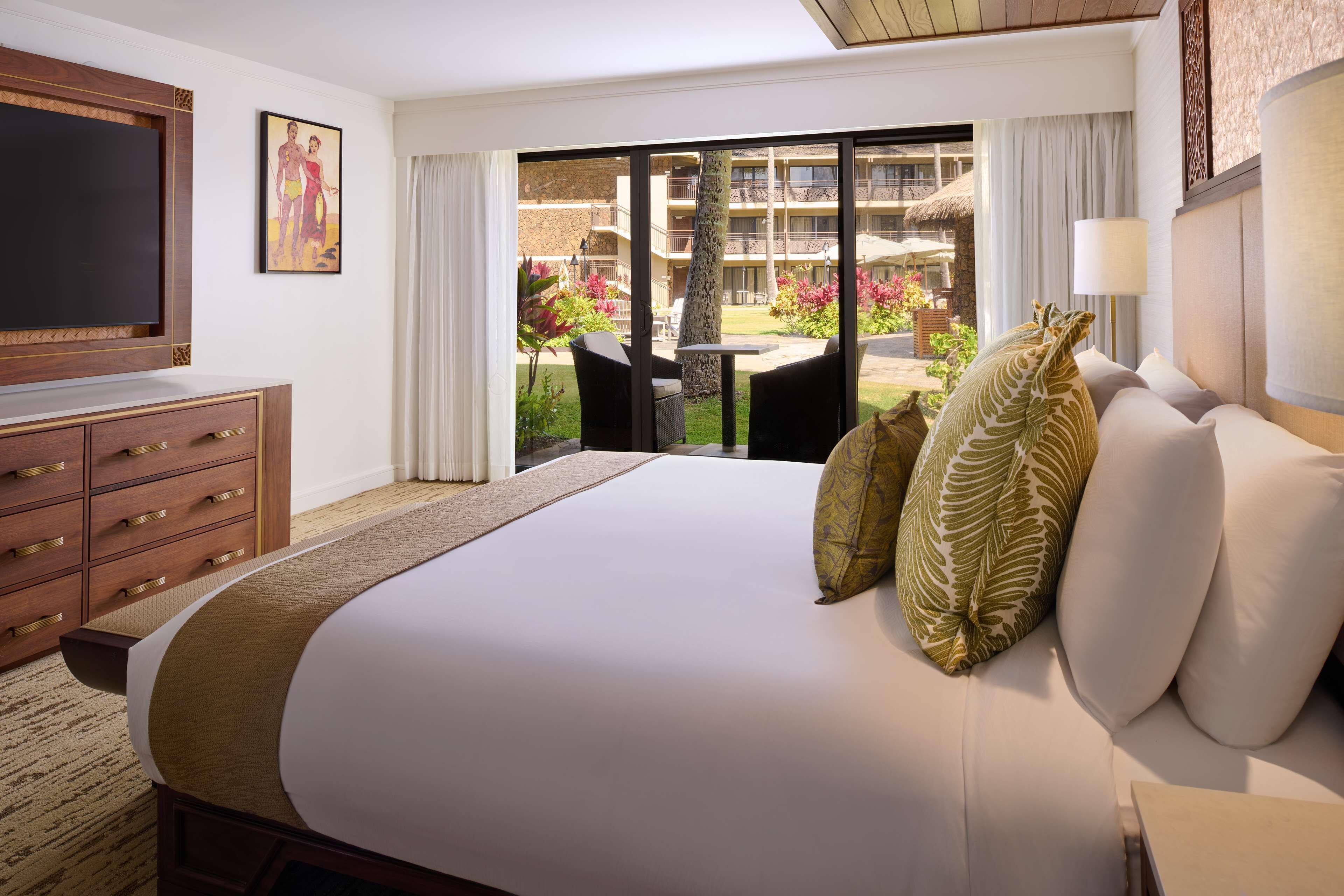 Quarto de hotel com uma cama grande, televisão, escrivaninha e vista para a área externa.