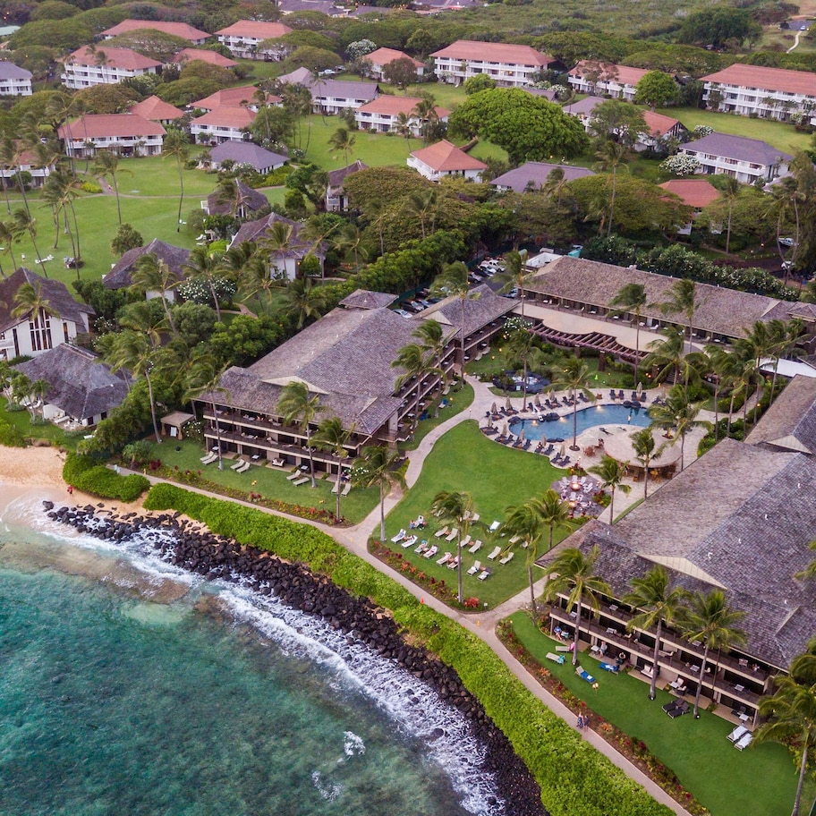 An aerial view of a resort with multiple buildings, a beach, and a swimming pool.