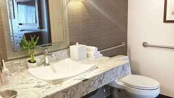A modern bathroom with a marble sink, a toilet, a mirror, and a wall-mounted light fixture.