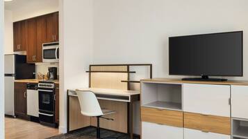 A modern kitchen with a microwave, stove, and coffee maker. There is a desk with a chair and a television on a stand.