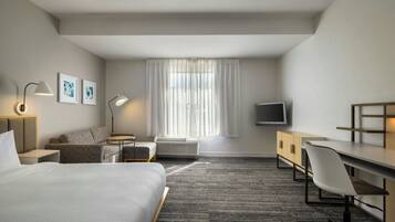 Une chambre d’hôtel avec un lit, un bureau, une chaise, une télévision et une fenêtre avec des rideaux.