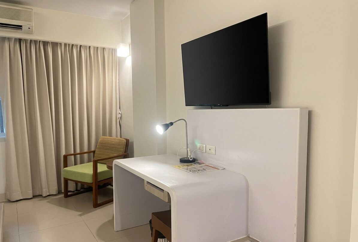 Een kleine kamer met een bureau, stoel, televisie en gordijnen.