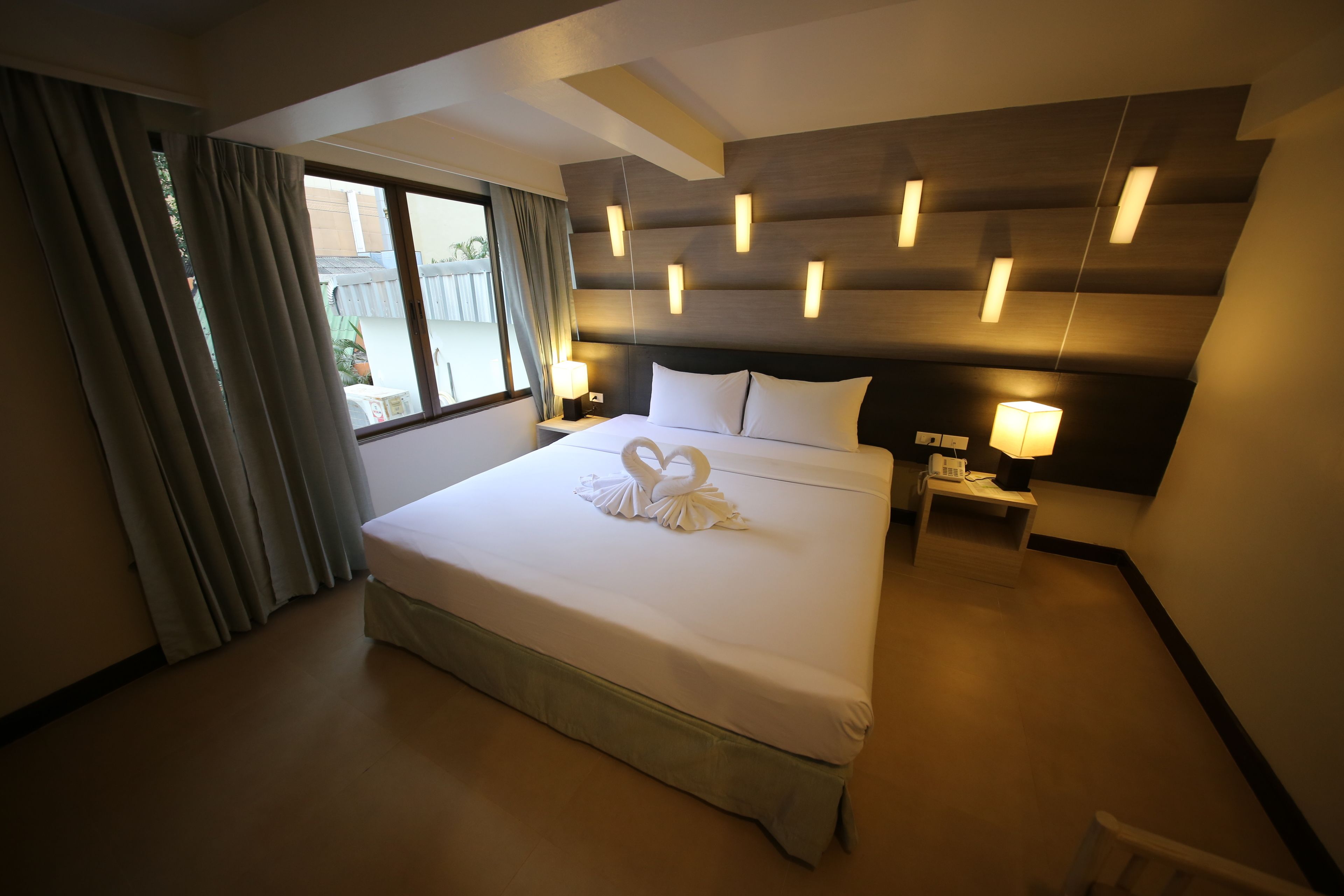 Una camera d'albergo con un letto grande, un comodino con una lampada e vista sull'esterno dalla finestra.