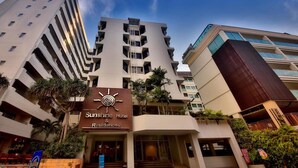 A hotel with a modern design, featuring a prominent sun symbol on the facade, multiple balconies, and a well-maintained garden area. - Sunshine Hotel And Residences (Pattaya)