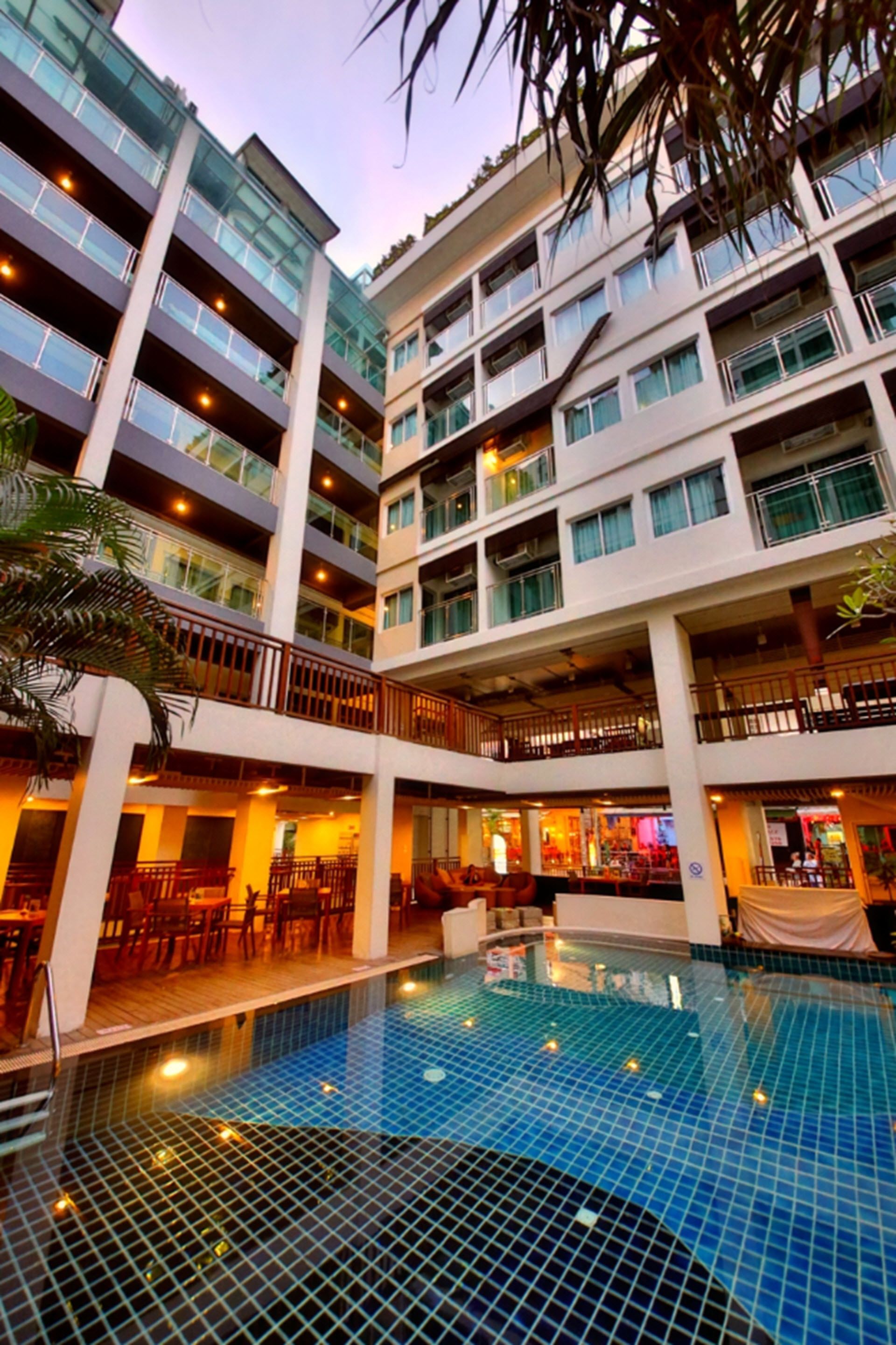 Un hotel de varios pisos con un área de piscina central, varios balcones y un espacio interior para comer.