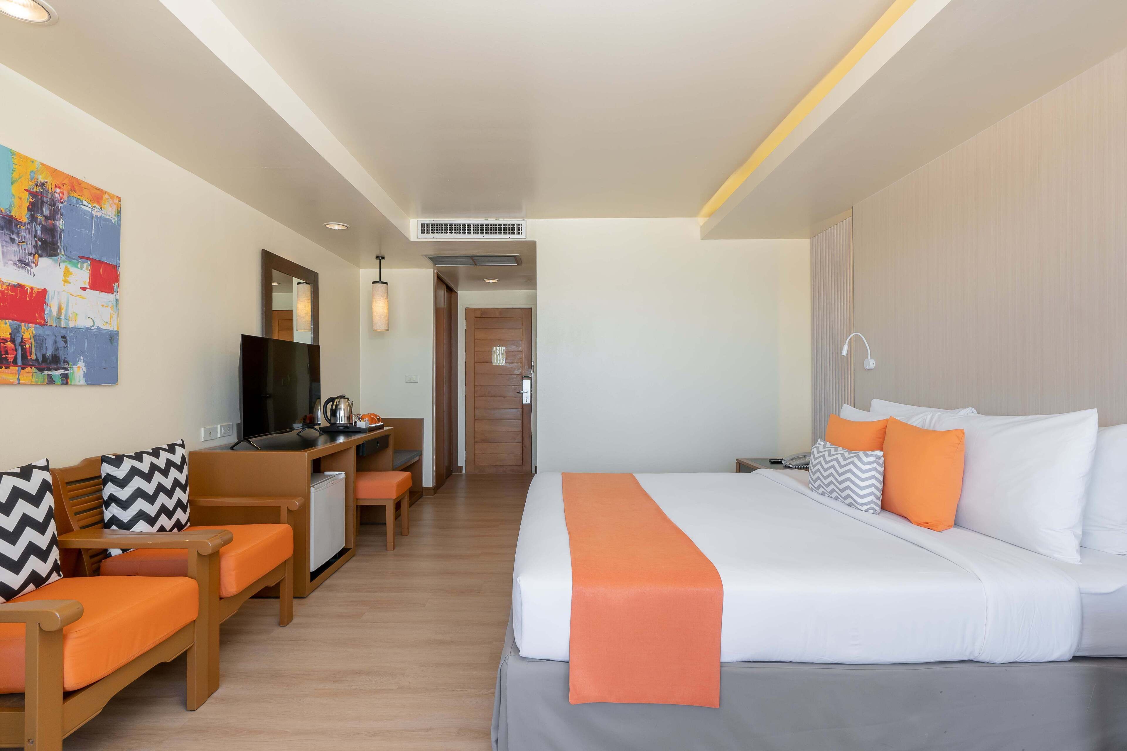A hotel room with a bed, a desk, a chair, a television, and a painting on the wall.