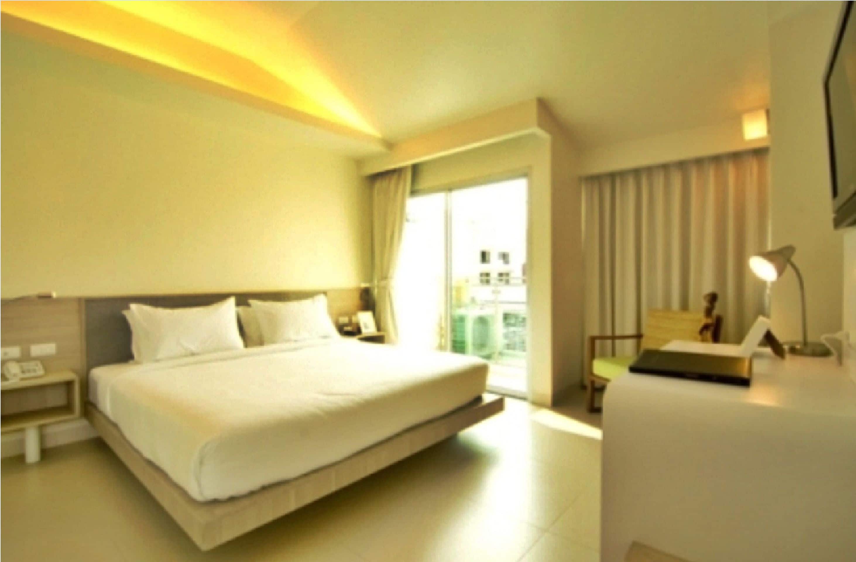 A hotel room with a large bed, bedside tables, a desk, a chair, and a view of the city through the window.