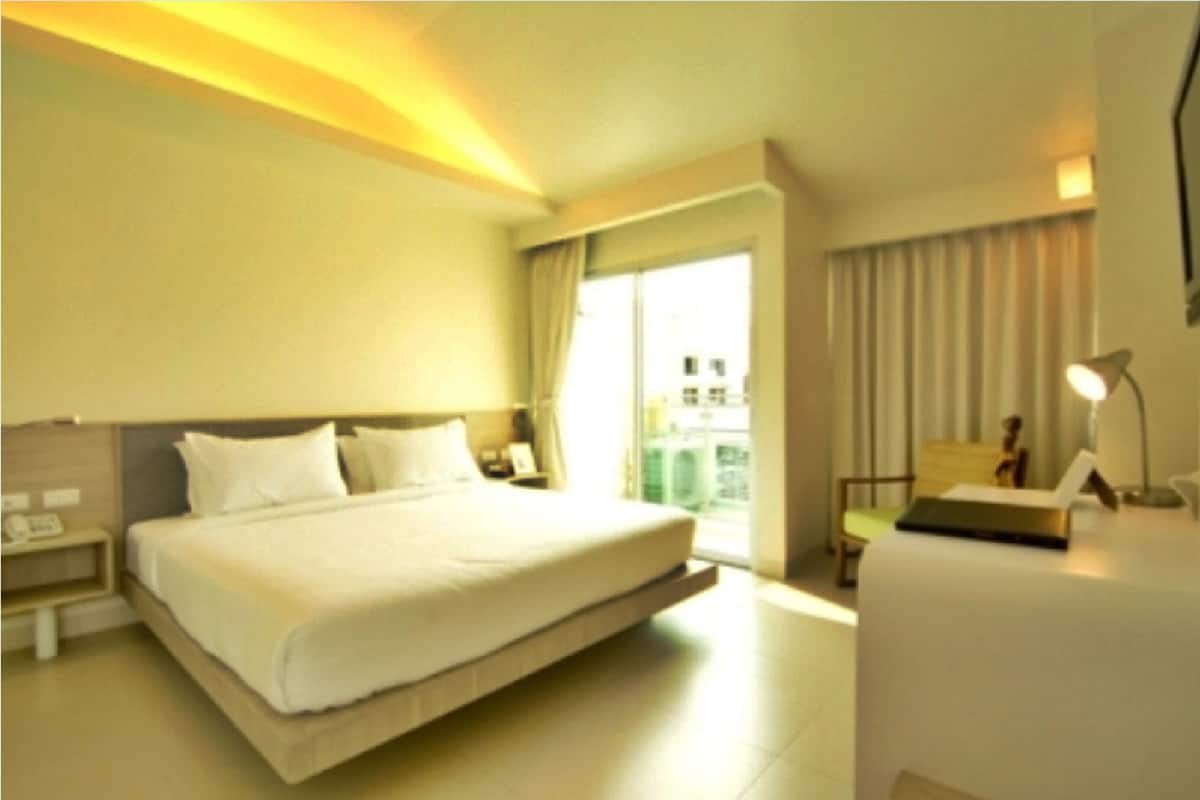 A hotel room with a large bed, bedside tables, a desk, a chair, and a view of the city through the window.