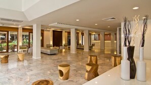 A spacious lobby with a high ceiling, marble flooring, wooden stools, and modern vases. - Sunshine Hotel And Residences (Pattaya)