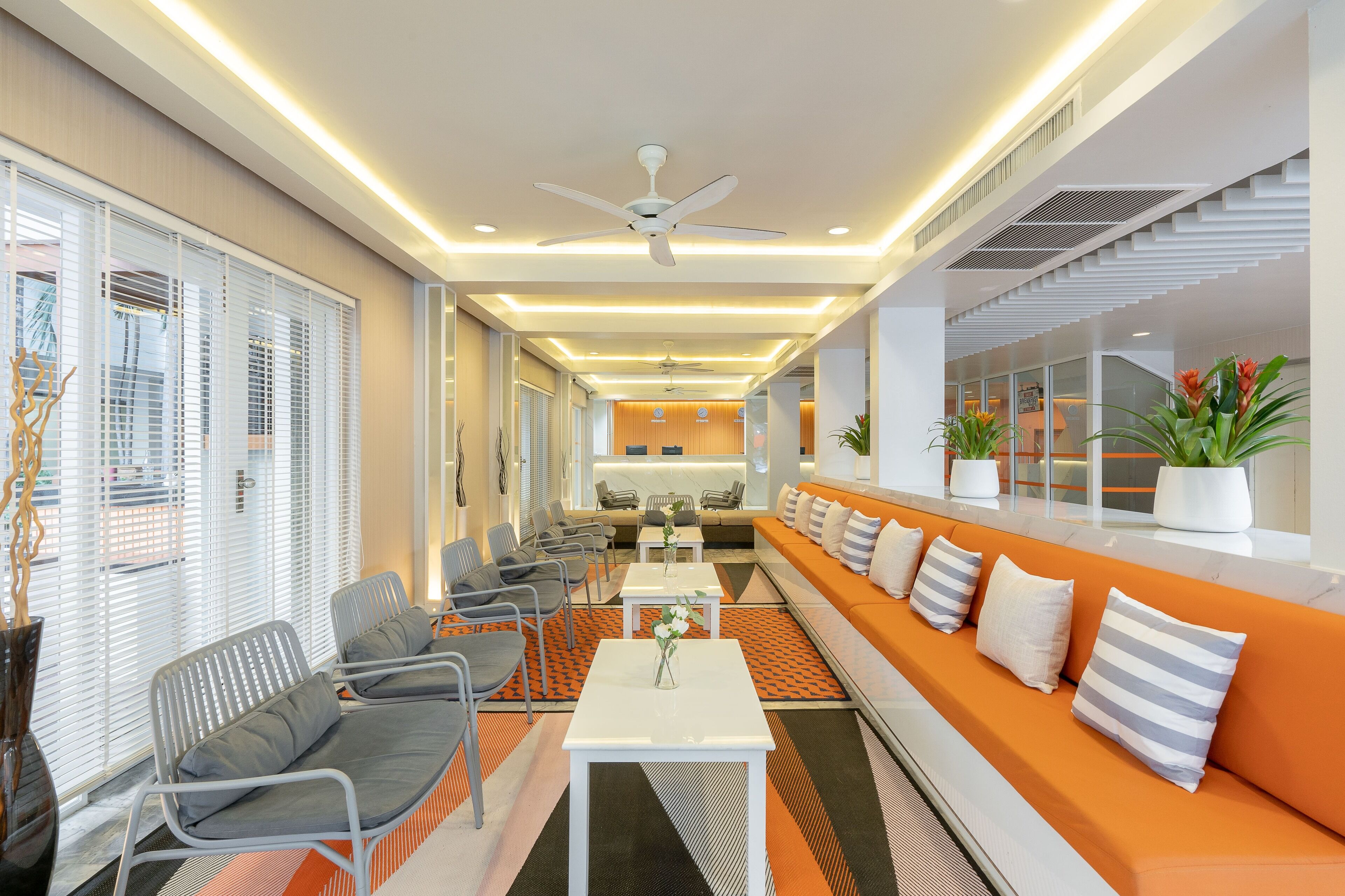 Un hall d’hôtel moderne, doté d’espaces aménagés avec des sièges, d’un comptoir d’accueil et d’un escalier.