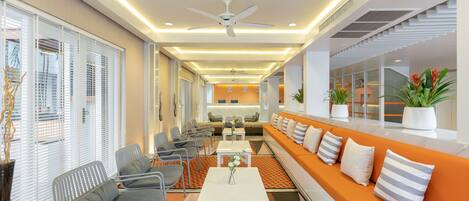 A modern hotel lobby with seating areas, a reception desk, and a staircase.