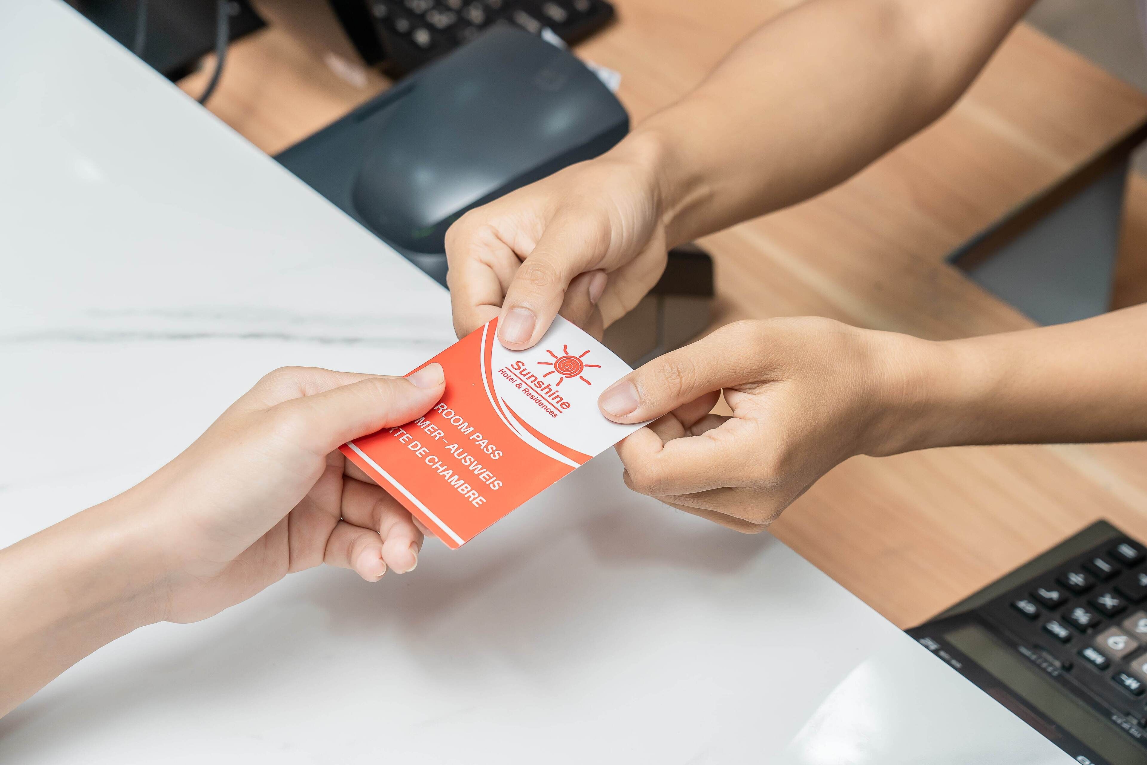 A person handing over a room pass to another person at a desk.