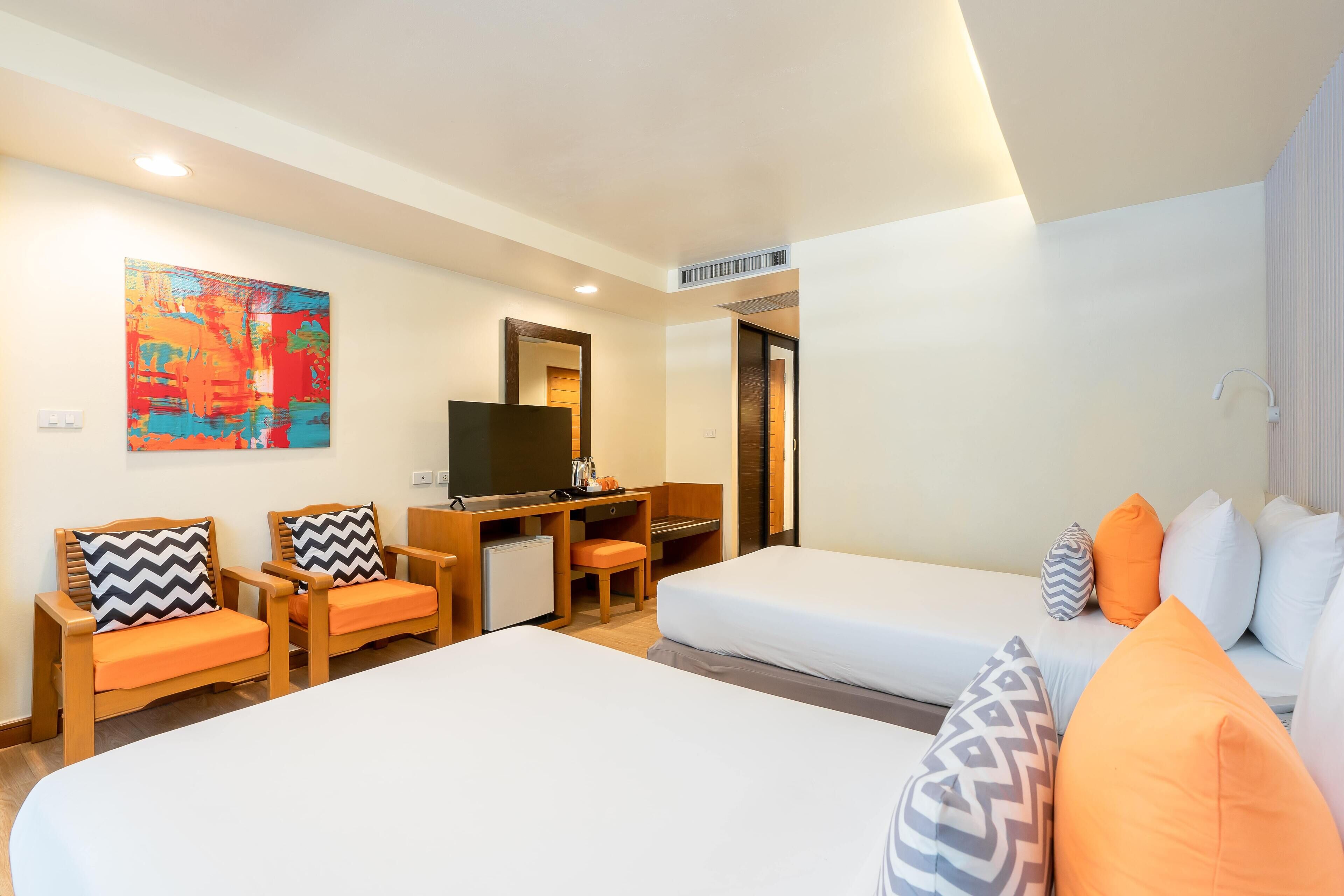 A hotel room with two beds, a desk with a TV, a small seating area, and a colorful abstract painting on the wall.