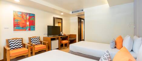 Quarto de hotel com duas camas, uma mesa com televisão, um espaço de estar pequeno e um quadro abstrato colorido na parede.
