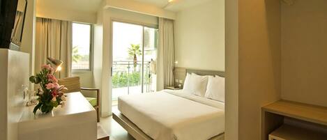 A hotel room with a bed, a desk with a lamp, a small table with flowers, a balcony with a view, and a control panel.