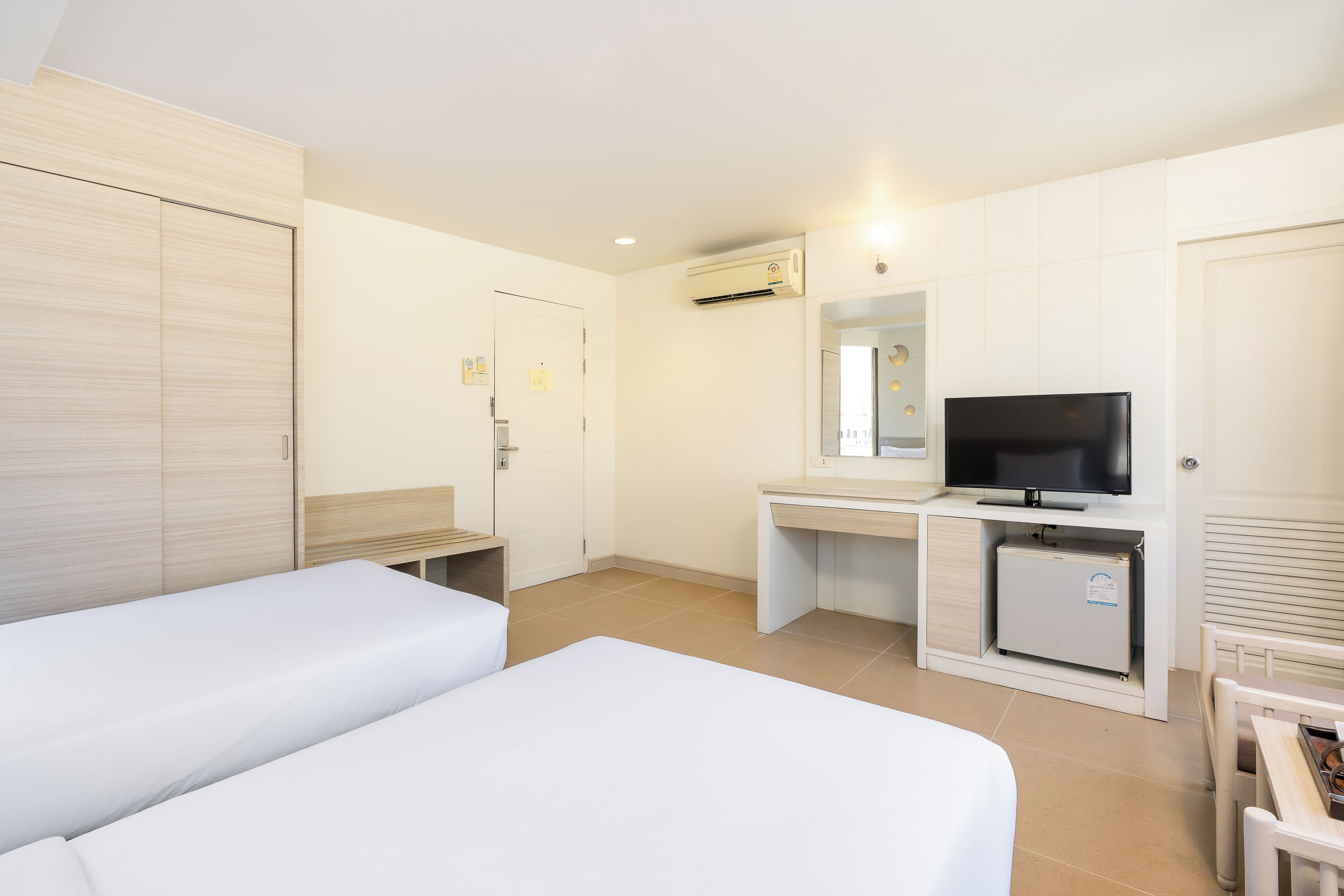 Une chambre d’hôtel avec deux lits, un bureau avec une télévision, un mini-réfrigérateur et un appareil de climatisation.