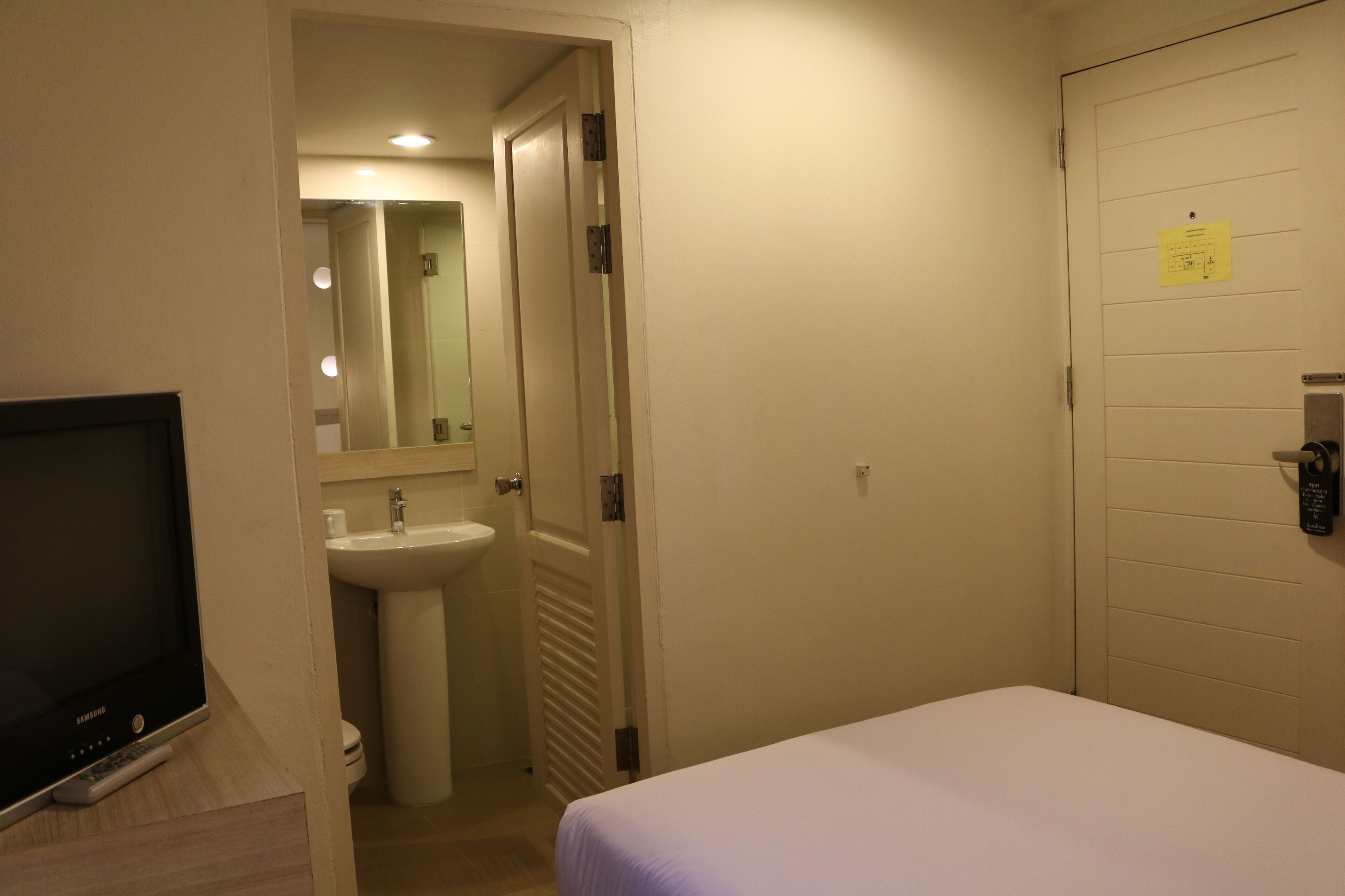 A hotel room with a bed, a television, a sink, and a mirror.